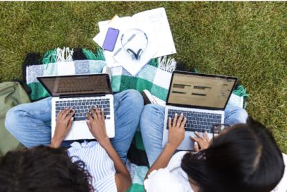 two women outside, working on their laptops