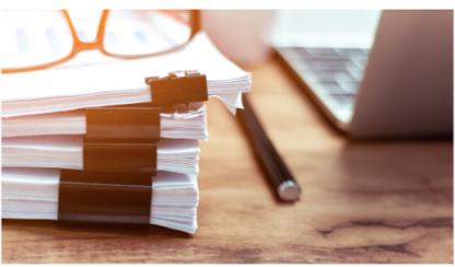 stack of papers on table with glasses and laptop